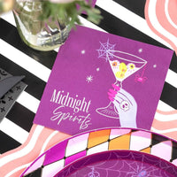 Halloween tablescape with a folded Midnight Spirits cocktail napkin, purple harlequin accents, and a pink swirl placemat on a black and white striped runner