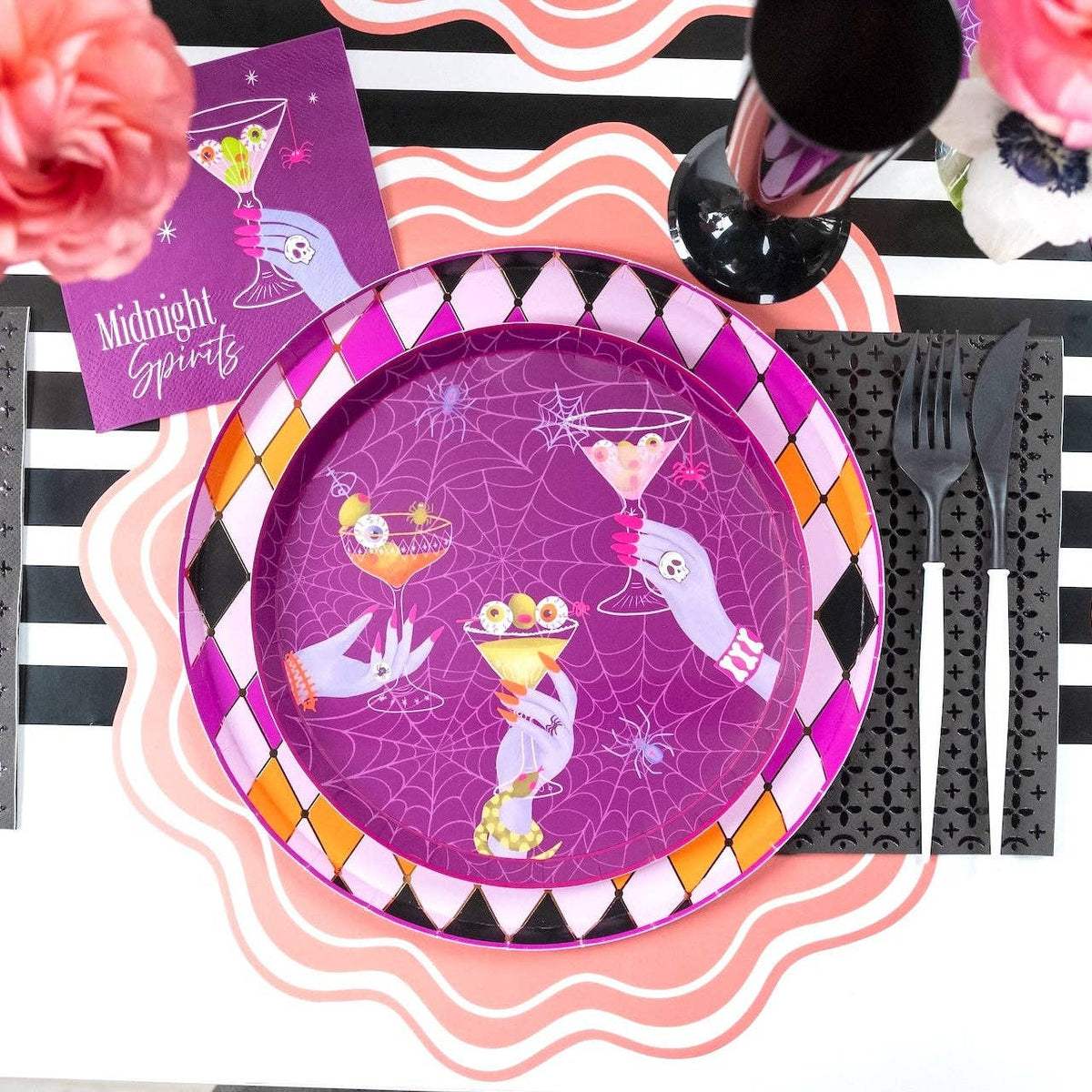Overhead Halloween place setting with a purple Midnight Spirits plate showing the eyeball martini and hand design, pink scalloped edge, black diamond border, and black flatware