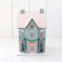 Mint Christmas village paper house with a pink glitter roof, two chimneys, and bottle brush trees by the front door