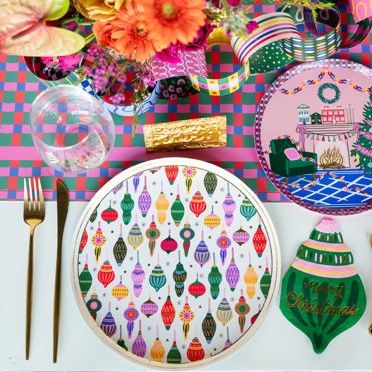 Vibrant Christmas dinner party table setting featuring the pink and teal checkered paper guest towels alongside colorful ornament shaped napkins and gold flatware.