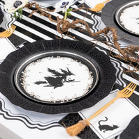 Wide tablescape view highlighting a modern gothic Halloween party setup with black die-cut chargers, witch plates, and cat silhouette napkins.