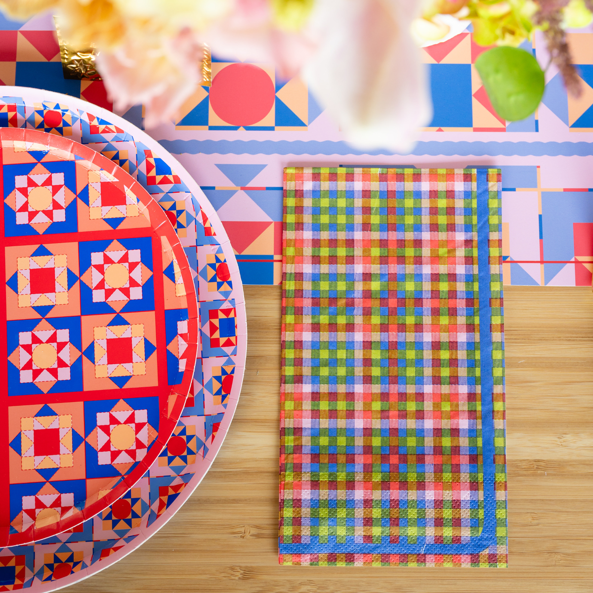 Layered holiday place setting showing the colorful plaid paper napkin resting next to a vibrant geometric tile patterned paper plate.