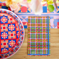 Layered holiday place setting showing the colorful plaid paper napkin resting next to a vibrant geometric tile patterned paper plate.