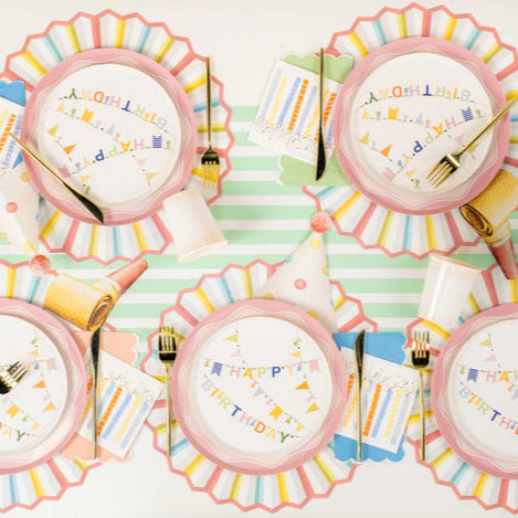 Overhead birthday table with pastel plates, party hats, and candle print beverage napkins at each place.
