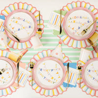 Overhead birthday table with pastel plates, party hats, and candle print beverage napkins at each place.