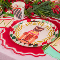 Close table angle with greenery and berries beside nutcracker plates and cups.