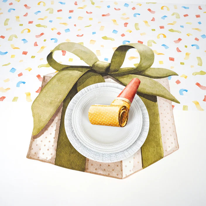 Place setting styled on a confetti table runner with a painted gift box and green bow under a white plate and party blower.
