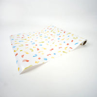 Partially unrolled confetti paper runner lying at an angle on a white surface.