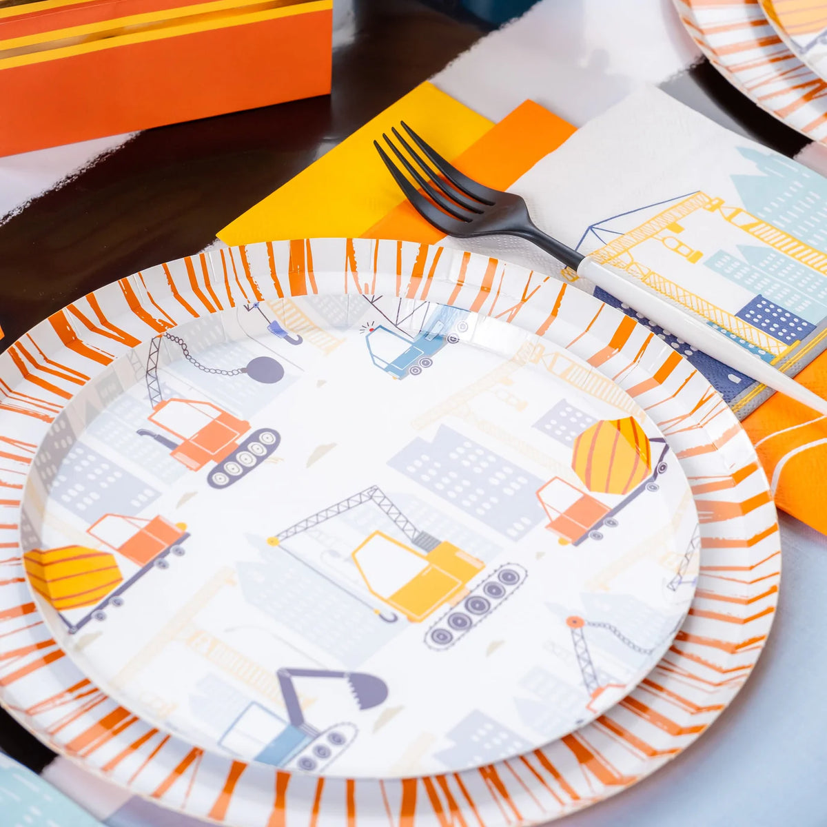 Angled place setting showing construction dessert plate beside fork and napkin.