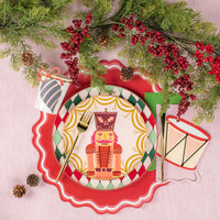 Holiday place setting with multicolor diamond rim dinner plate, nutcracker center plate, red scalloped placemat, and greenery.