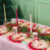 Long holiday table styled with diamond rim plates, candles, and paper trees in the background.