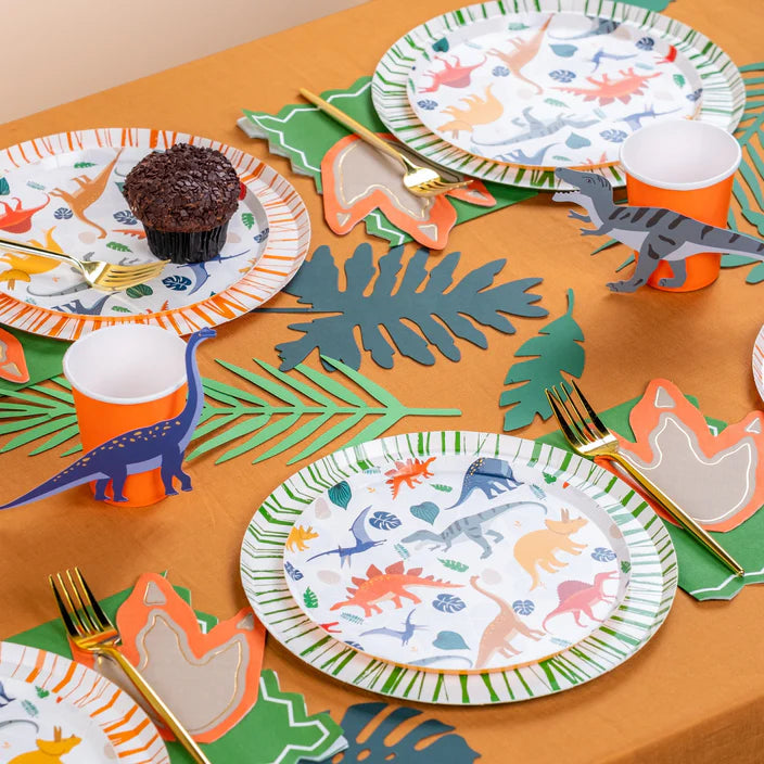 Wide party table with multiple dino place settings and scattered accent stickers.