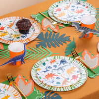 Wide party table with multiple dino place settings and scattered accent stickers.