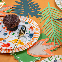 Cupcake on stacked plates with green leaf runner and dino footprint napkin.