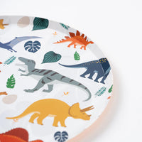 Close up of dinosaur dessert plate with T Rex, Stegosaurus, and leaves on white.