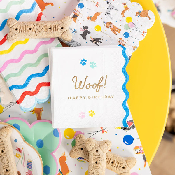 Close overhead of Woof birthday napkin stacked with dog party cocktail napkins and dog bones.