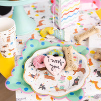 Dessert table with dog party plate, bone shaped cookies, cups, and colorful napkins.