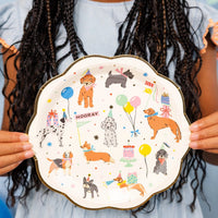 Person holding a dog party plate showing multiple illustrated dogs in party hats.