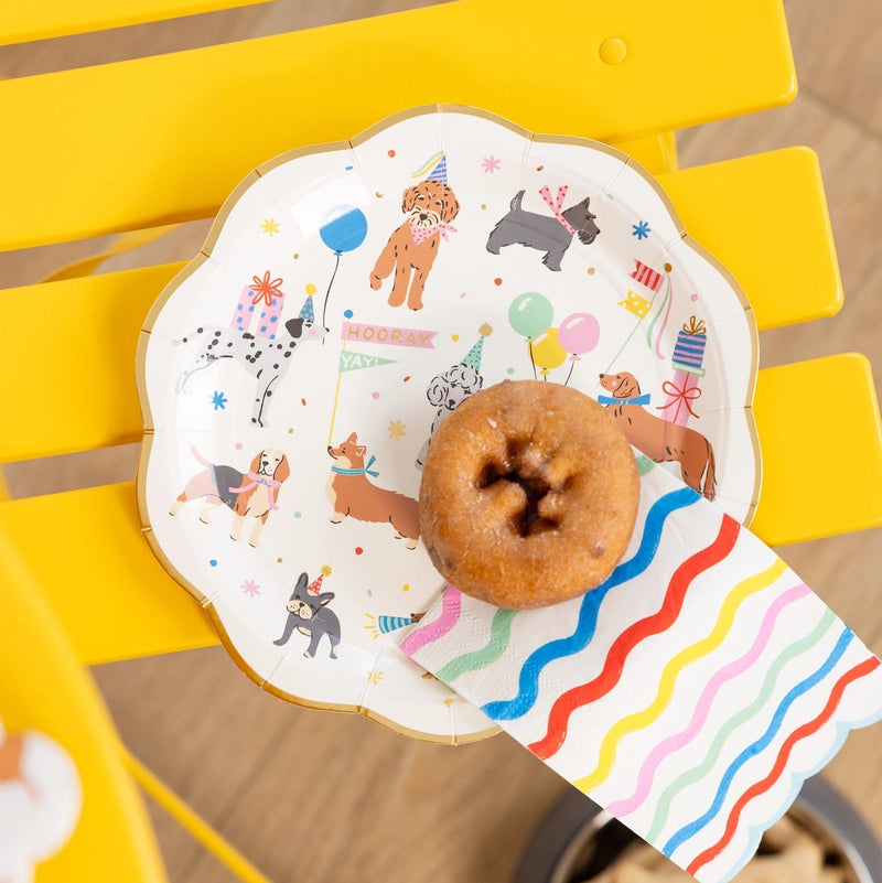 Dog party plate on a bright yellow chair with a donut and rainbow napkin.