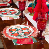 Place setting with dot print dessert plate, gold cutlery, red glass, and paper trees in the background.