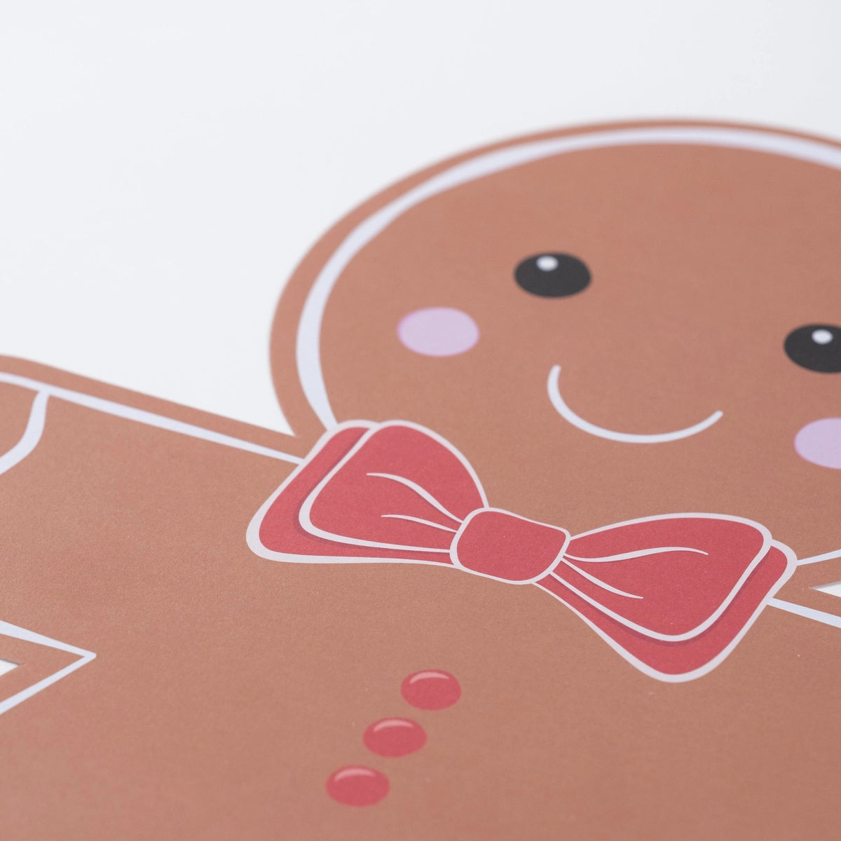 Closeup of gingerbread face with pink cheeks and red bow tie on paper placemat.