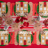 Overhead table layout with multiple gingerbread placemats, square house plates, and red florals.