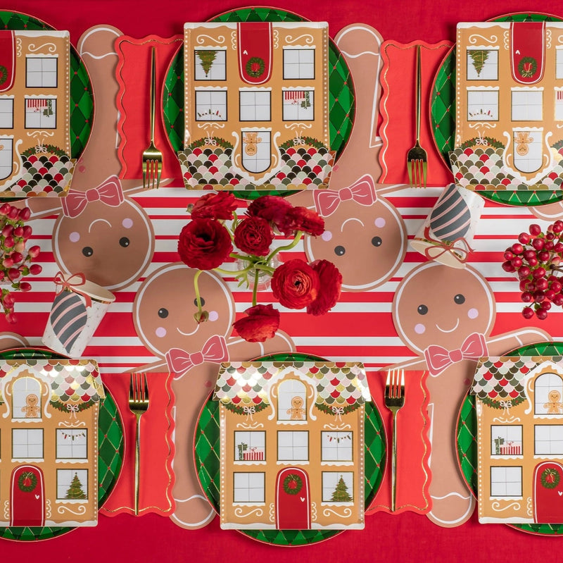 Overhead table layout with multiple gingerbread placemats, square house plates, and red florals.