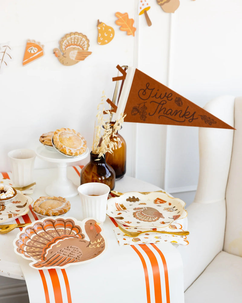 Fall buffet table with pies and leaf garland, Give Thanks pennant displayed in a vase.