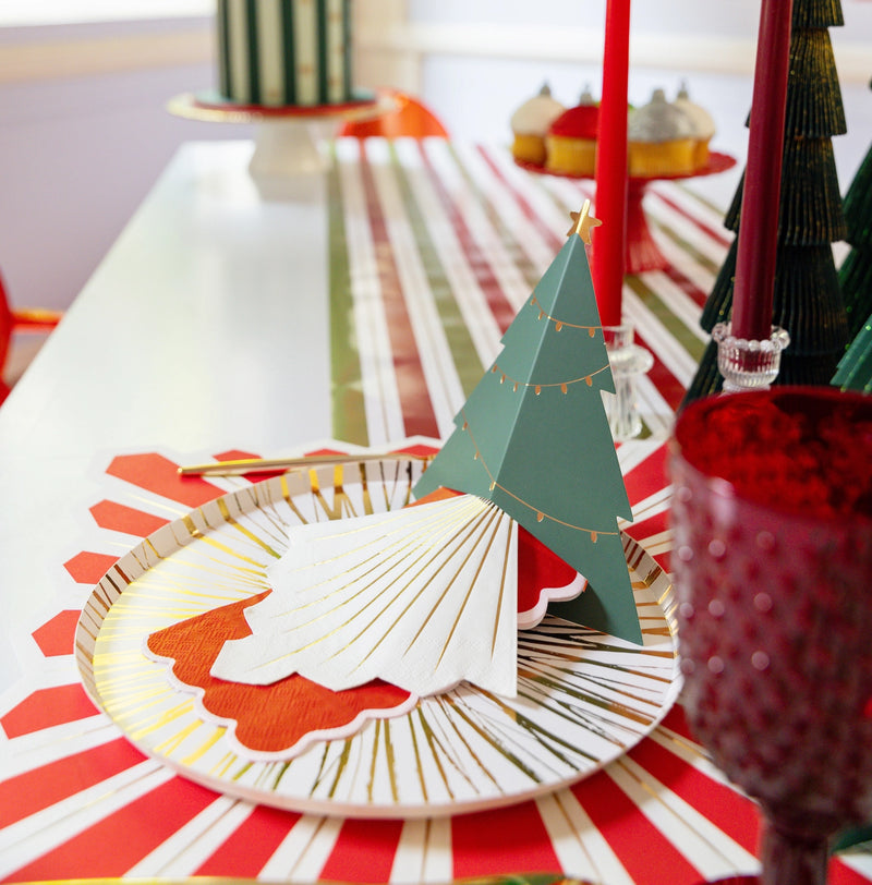 Holiday table place setting with white napkin that has gold rays layered on a plate.