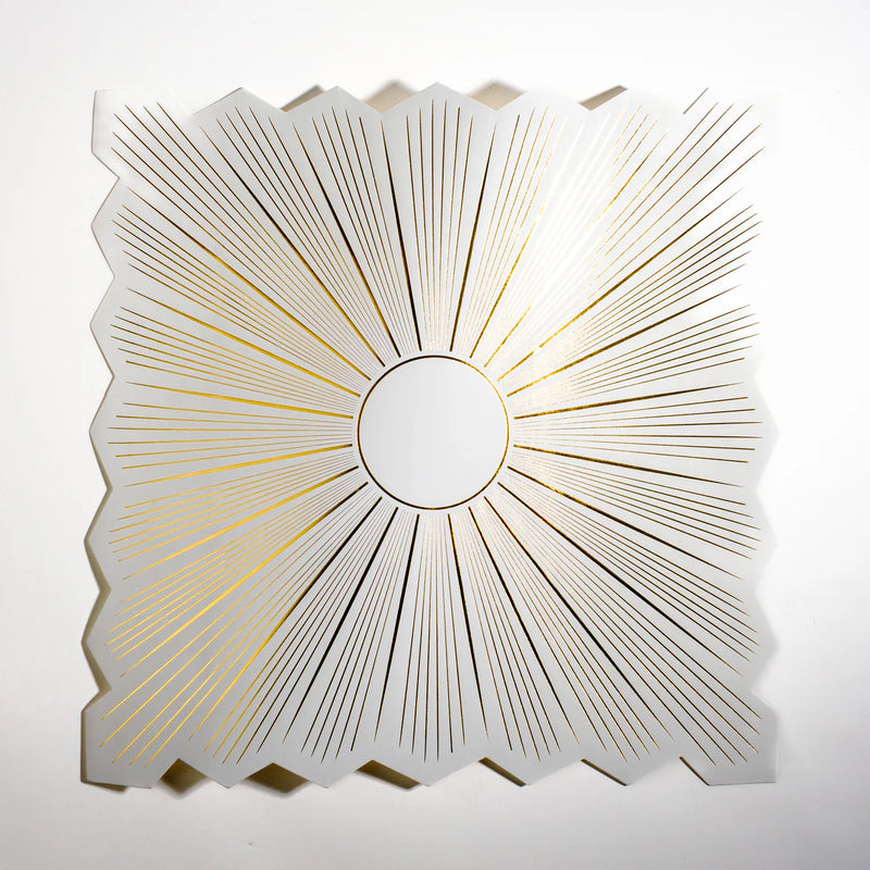 Top down of white square placemat with gold starburst and zigzag edge.