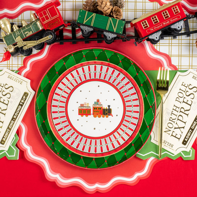Place setting with green diamond dinner plate and red trimmed center plate beside train decor.