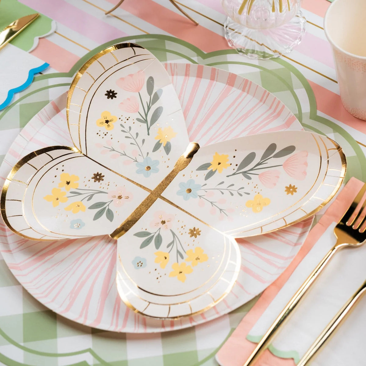 Close view of butterfly plate layered on green gingham placemat with gold flatware.