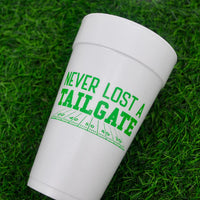 White 20 ounce foam cup with green Never Lost a Tailgate text lying on artificial turf.