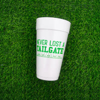 Full view of white foam cup with green Never Lost a Tailgate graphic centered on turf background.