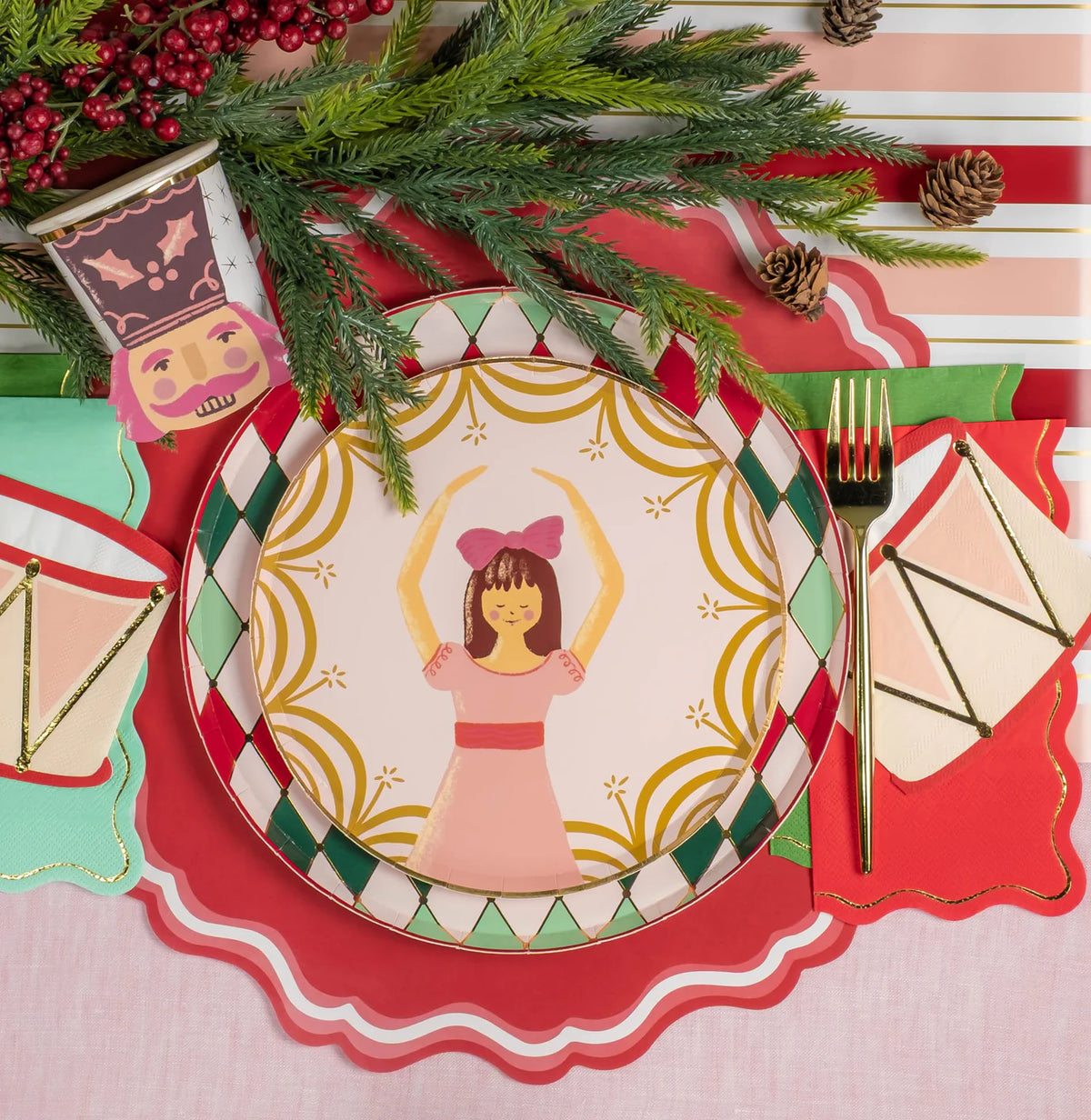 Single place setting with ballerina plate, drum napkin, and nutcracker cup near evergreen sprigs.