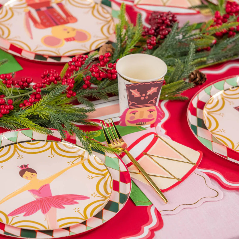 Close view of place settings with nutcracker cups and ballerina plates on a red runner.
