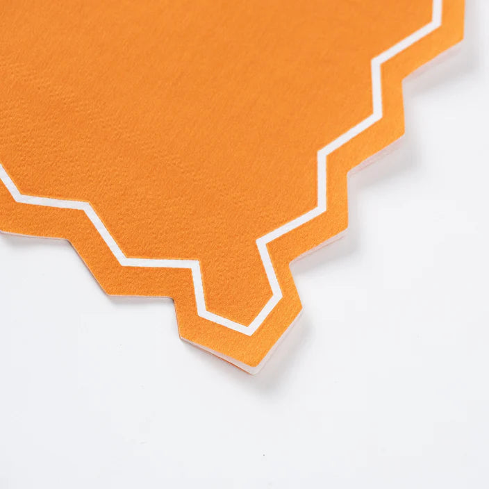 Closeup of orange guest towel corner with zigzag scalloped edge and white outline.