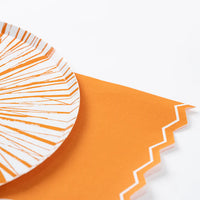 Orange guest towel styled under a white plate with orange splash stripes.