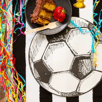 Large soccer placemat beneath a black plate of cake and party streamers.
