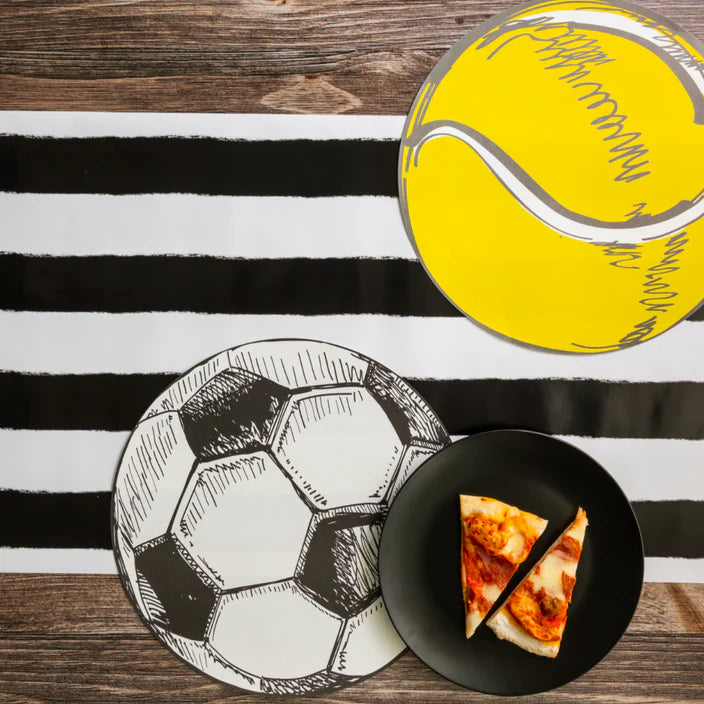 Soccer and tennis ball placemats on a black and white stripe runner with a plate of pizza.