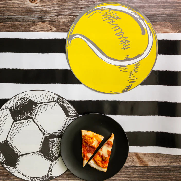 Yellow tennis ball and black and white soccer placemats on a striped runner with a plate of pizza.