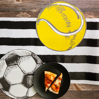 Yellow tennis ball and black and white soccer placemats on a striped runner with a plate of pizza.