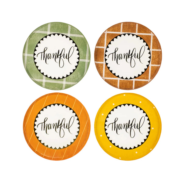 Styled close view of mustard “thankful” plate on plaid dinner plate with pumpkins and leaf napkin.