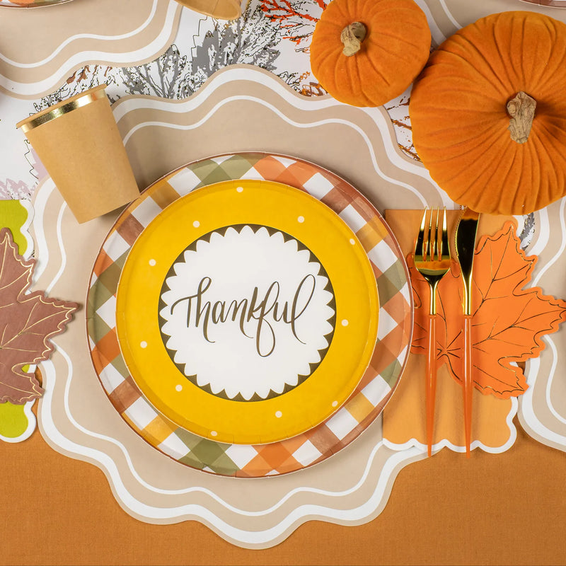 Place setting with mustard “thankful” dessert plate layered on harvest plaid dinner plate with pumpkins nearby.