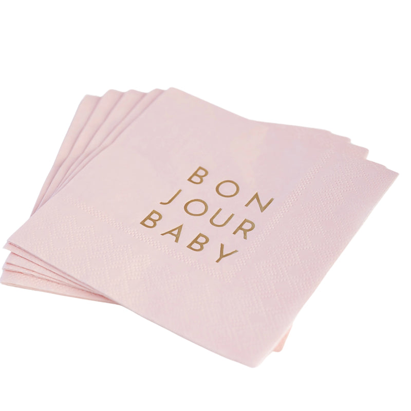 Stack of blush pink cocktail napkins with gold‑foil “Bonjour Baby” lettering styled for baby girl shower.