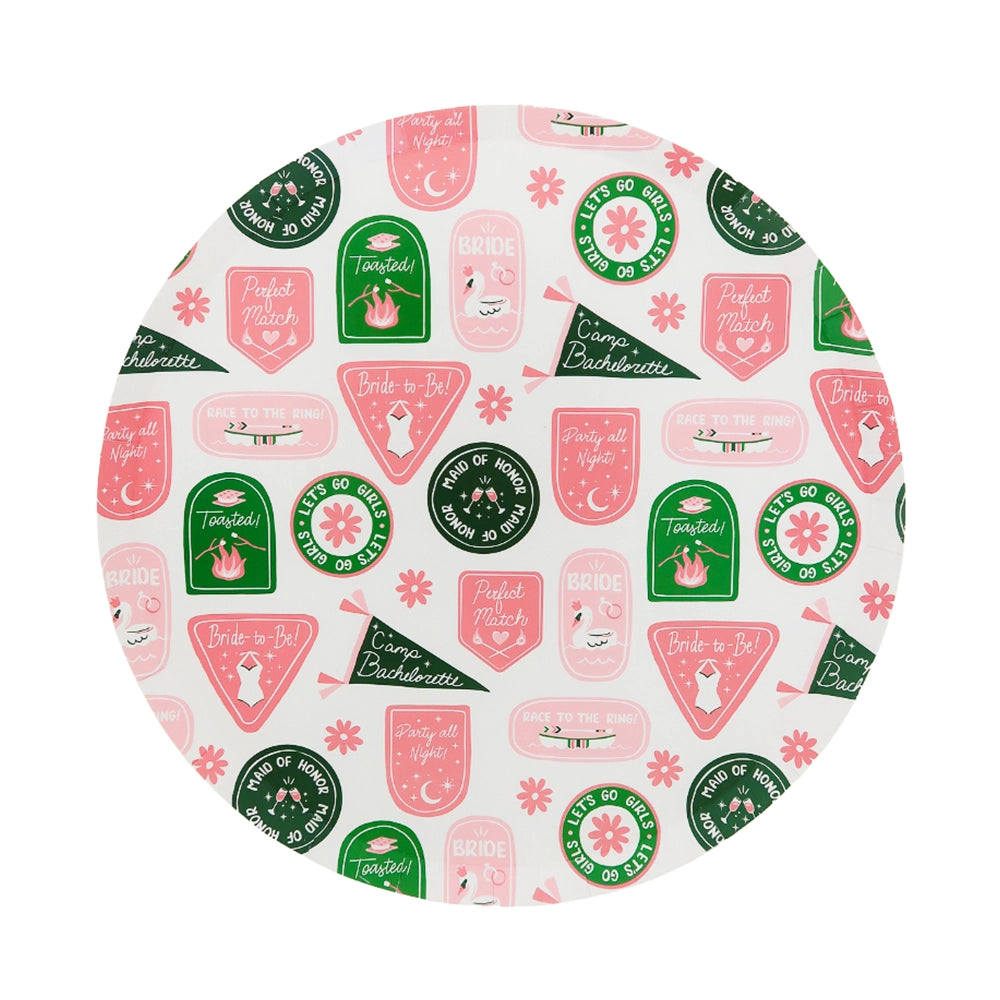 Close-up of round Camp Bachelorette dinner plate featuring pink and green badge illustrations