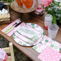 Rustic picnic table set with Camp Bachelorette badge dinner plate, matching napkins, pink drinks and s’mores fixings