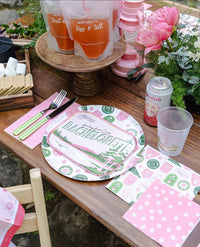 Overhead view of dinner setup featuring Camp Bachelorette badge plates and coordinating daisy napkins on wooden table