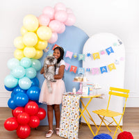 Girl holding fluffy cat beside pastel Cat Happy Birthday Banner and rainbow balloon arch