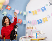 Woman playing with black-and-white cat under pastel Cat Happy Birthday Banner and balloons